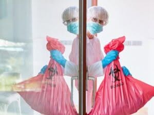 Un operatore con indumenti protettivi sta trasportando sacchi rossi contrassegnati per rifiuti biologici pericolosi, probabilmente per un'analisi rifiuti.