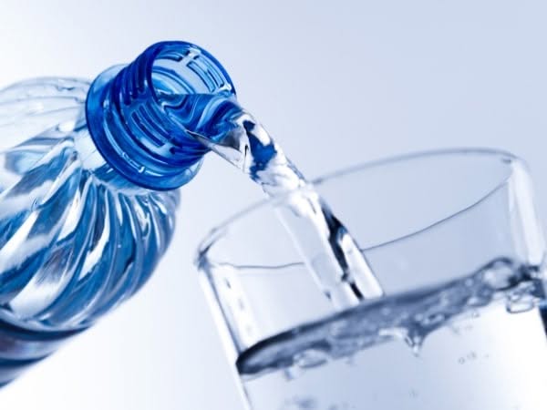 Una bottiglia di plastica blu che sta versando acqua potabile in un bicchiere trasparente.