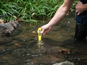  Un tecnico effettua un rilevamento ambientale campionando l'acqua in un corso d'acqua con un dispositivo giallo portatile.