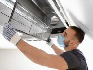 un uomo con mascherina sta installando un filtro in un sistema di ventilazione per migliorare l'inquinamento indoor